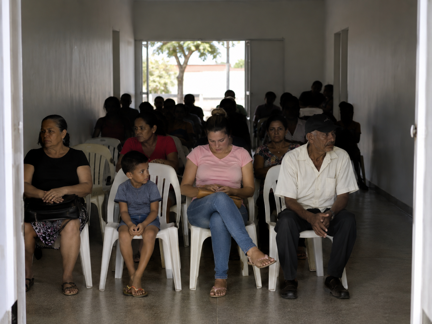 Sala de espera de unidade de saúde: as primeiras fileiras de cadeiras estão iluminadas e as pessoas nelas aparecem nítidas; as fileiras do fundo estão em penumbra e as pessoas ali são apenas silhuetas.